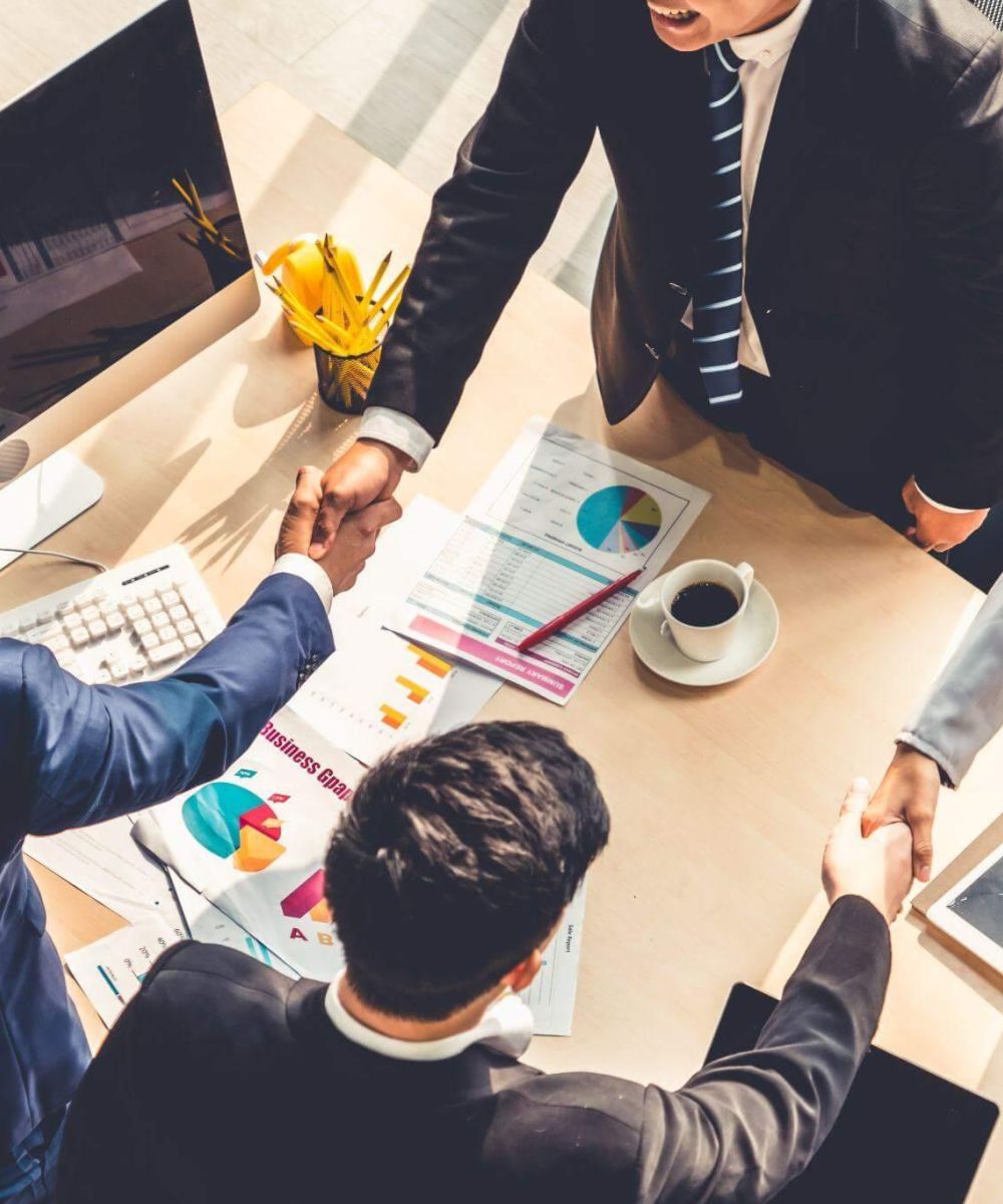 Business meeting with diverse professionals shaking hands over charts, reflecting collaboration and success.