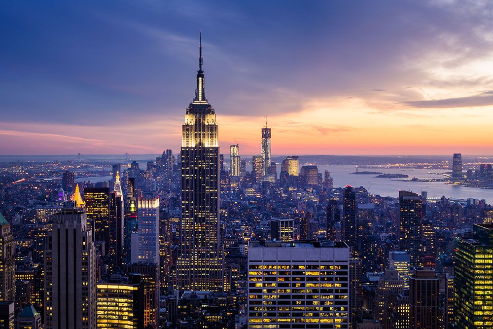 Aerial view of New York City skyline at sunset with iconic skyscrapers and vibrant cityscape lighting.
