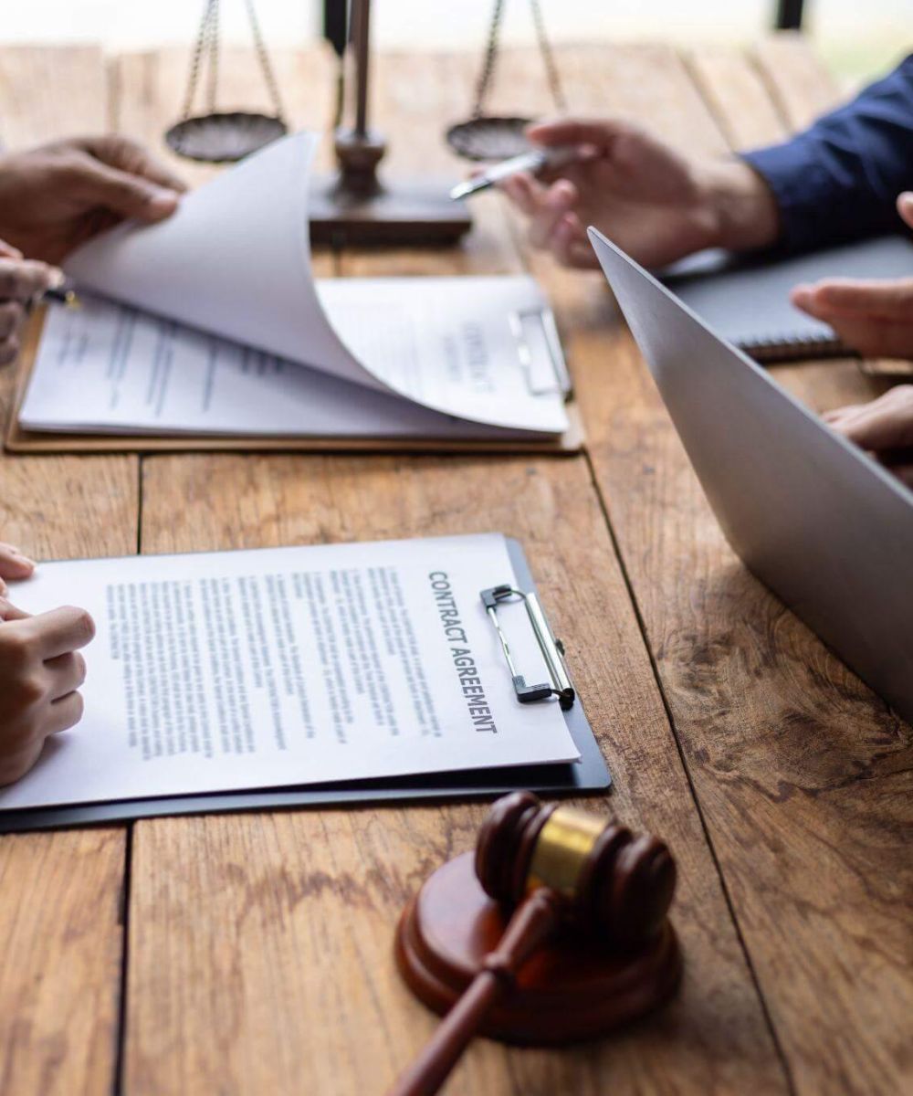 a group of people sitting around a wooden table and working with multiple documents and laptops