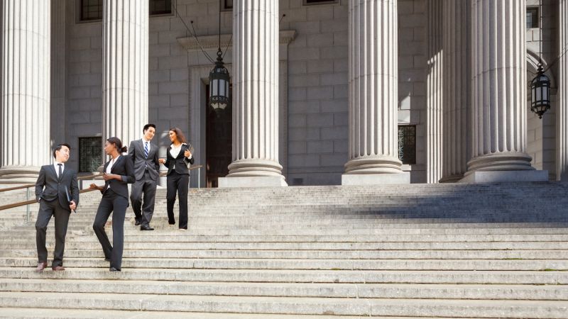 Business professionals walking down courthouse steps, discussing legal matters in formal attire.