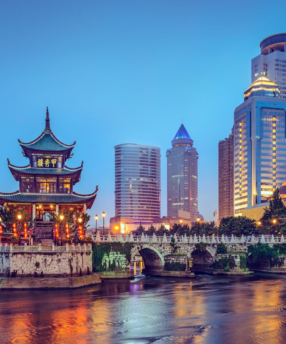 Scenic view of Guiyang's Jiaxiu Pavilion illuminated at dusk, surrounded by modern skyscrapers and a river bridge.