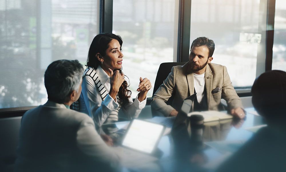 Business meeting in a modern office with diverse professionals engaged in discussion around a conference table.