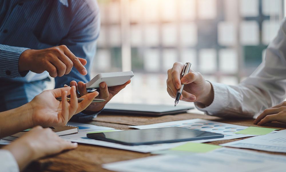 Business team analyzing charts and digital data on smartphones and tablets during a meeting in a well-lit office setting.