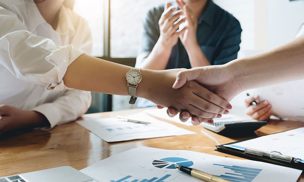 Business meeting handshake with charts on table, teamwork concept.
