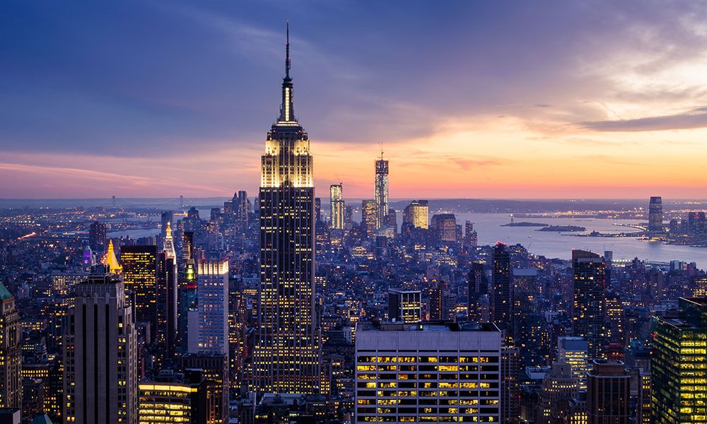 Aerial view of New York City skyline at sunset with iconic skyscrapers and vibrant cityscape lighting.