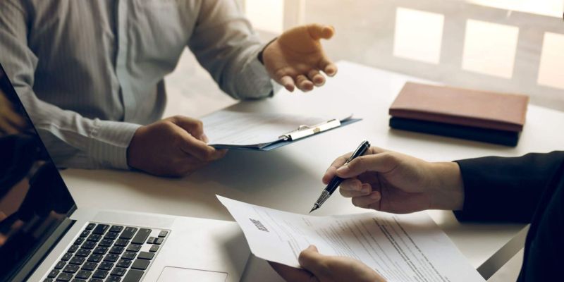two people sitting at a table with papers and a laptop
