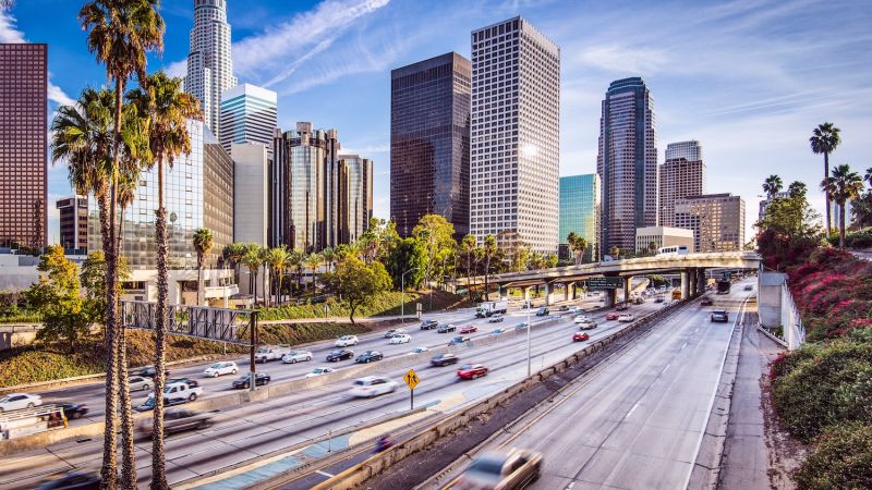 Bustling freeway with skyscrapers and palm trees under a clear blue sky in downtown Los Angeles.