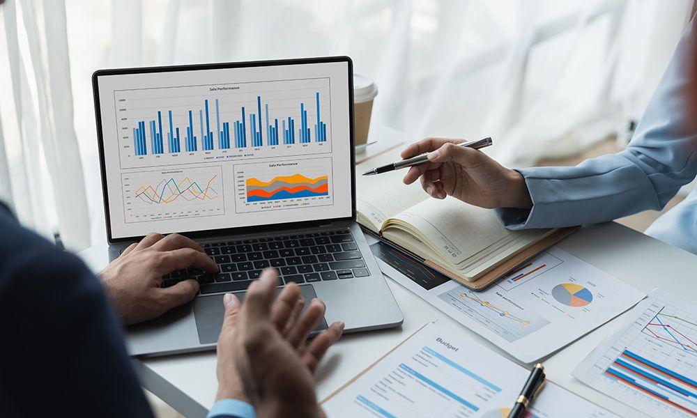 Business team analyzing charts on laptop and documents, discussing sales performance strategy.
