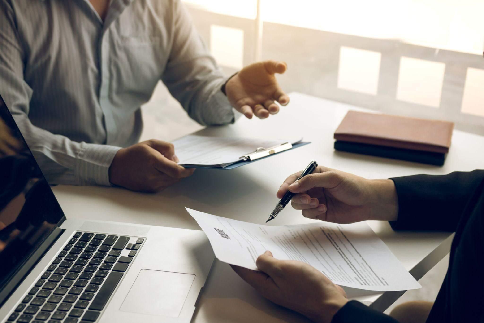 two people sitting at a table with papers and a laptop