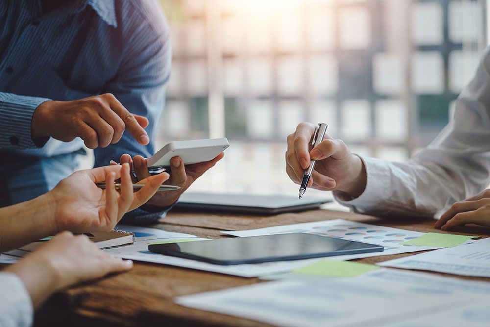 Business team analyzing charts and digital data on smartphones and tablets during a meeting in a well-lit office setting.