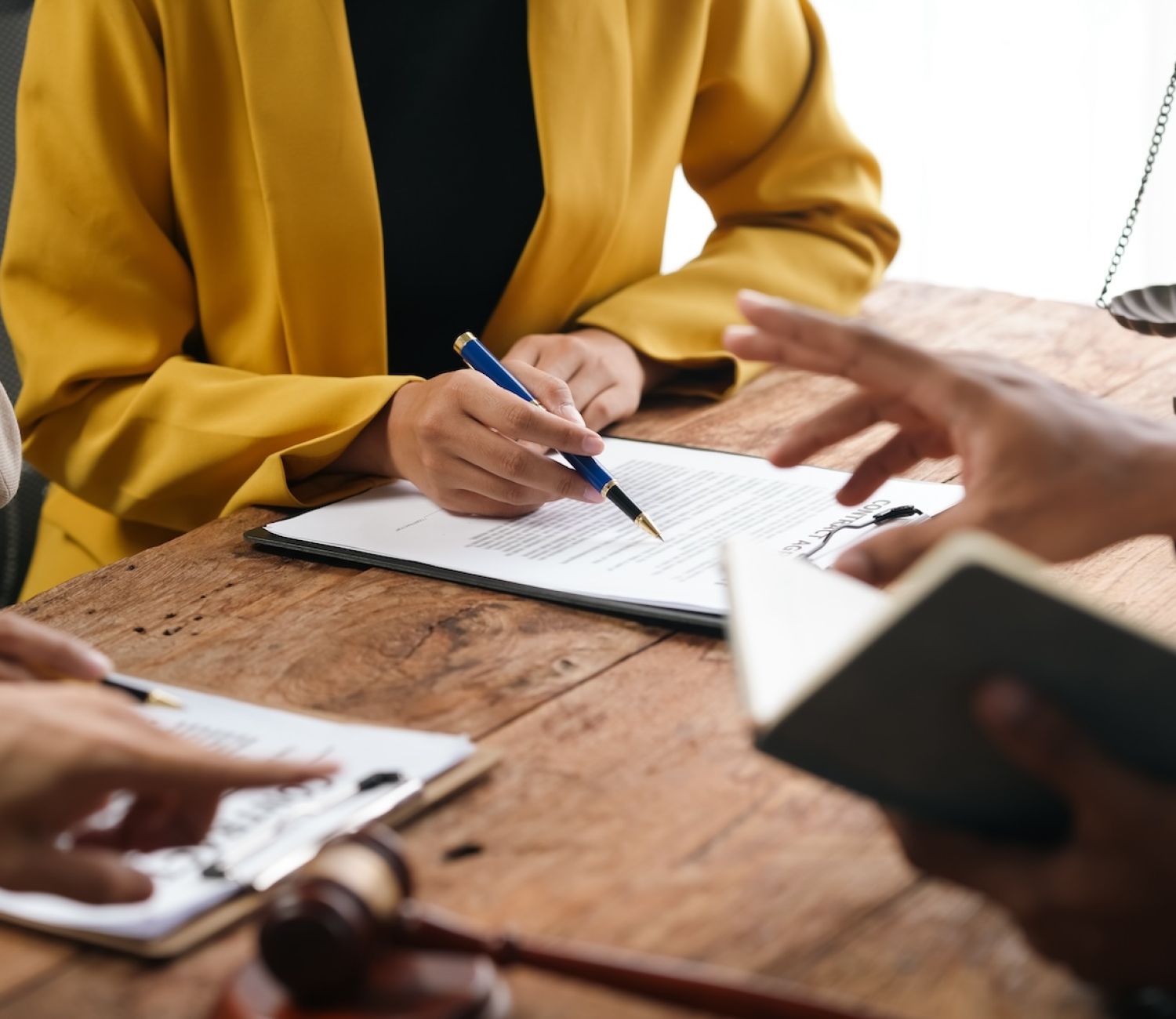People discussing and signing legal documents at a wooden table, featuring a gavel and scale of justice.