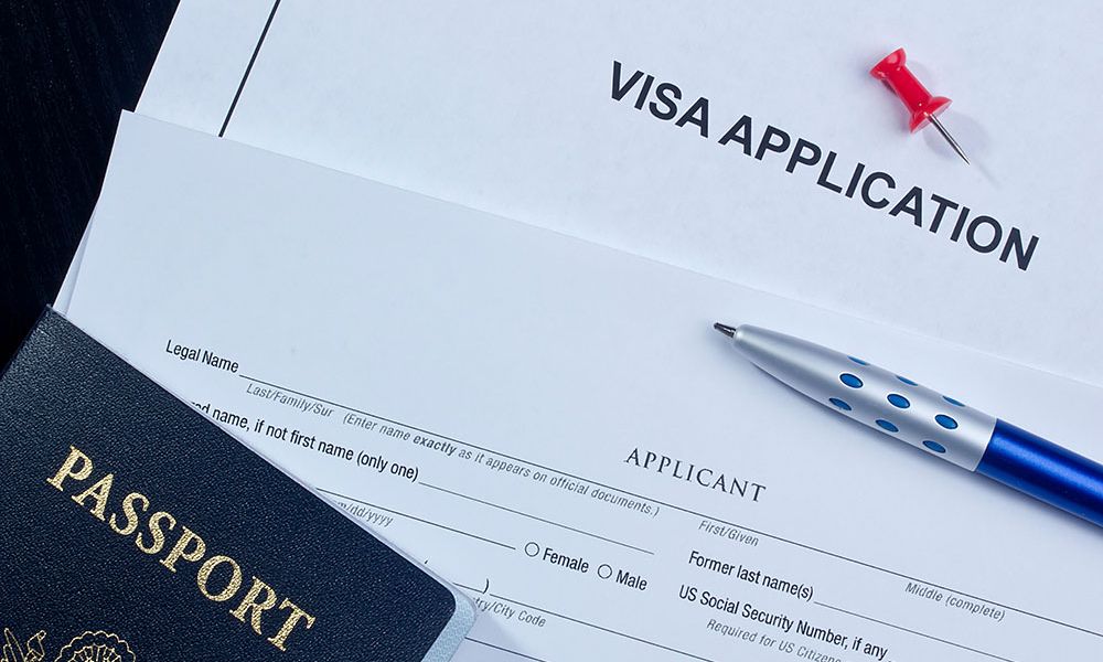 Visa application form with passport, pen, and thumbtack. Travel documents for visa processing.