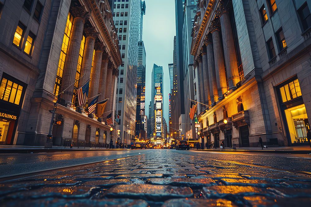 Downtown city street with illuminated buildings and wet cobblestones, flags hanging from columns, and a fading skyline.
