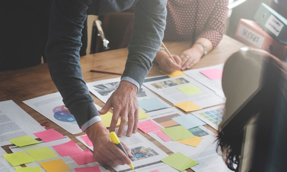 Team collaborating over documents and sticky notes in an office setting, planning strategy together.