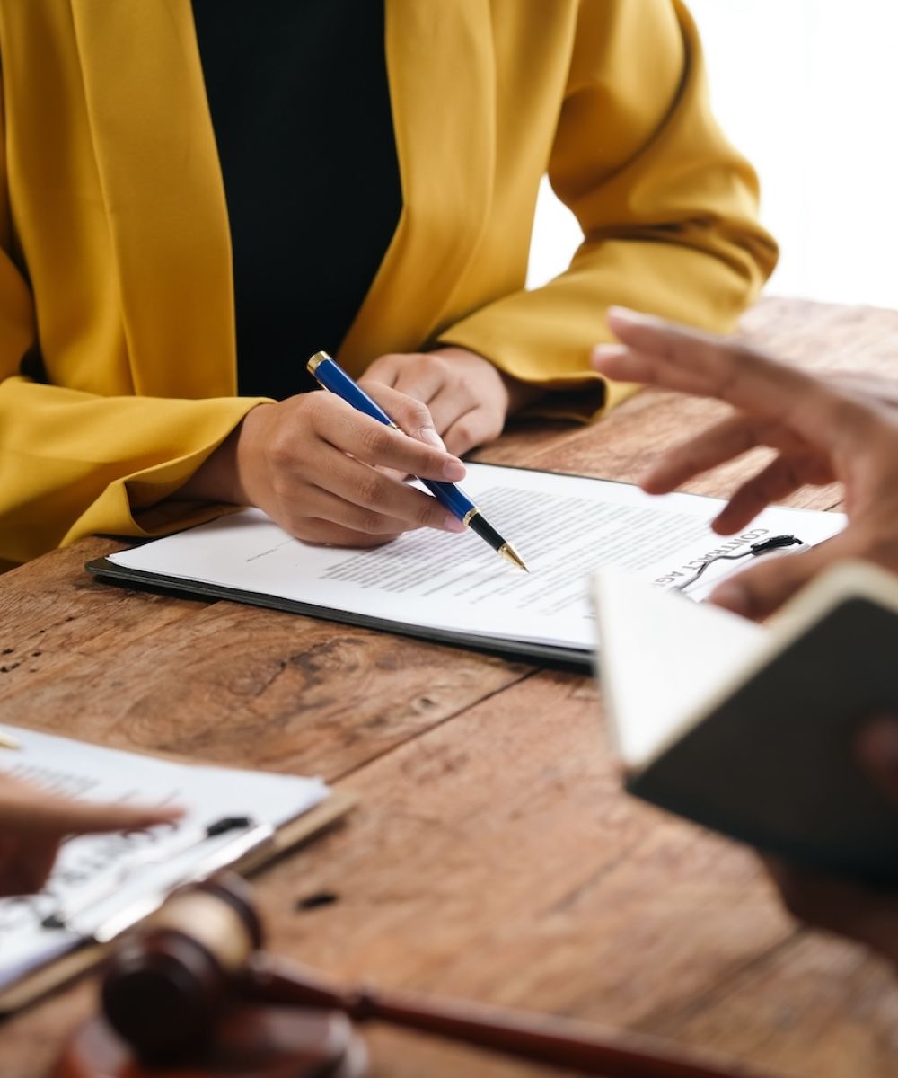 People discussing and signing legal documents at a wooden table, featuring a gavel and scale of justice.