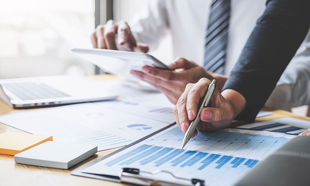 Business meeting with team analyzing financial graphs and using tablet.