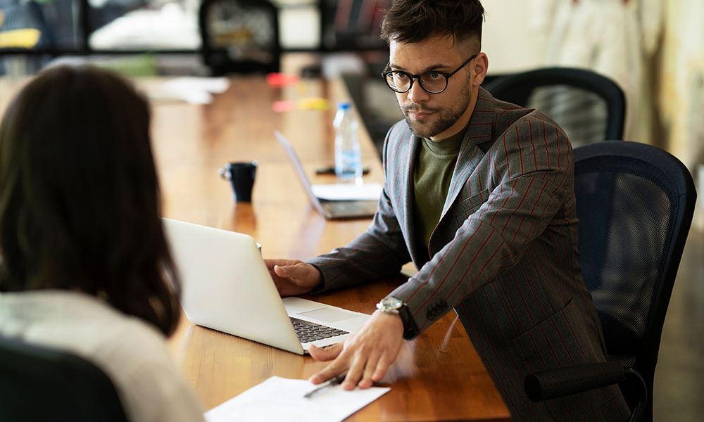 Man in glasses discussing documents with a colleague in a modern office meeting room.