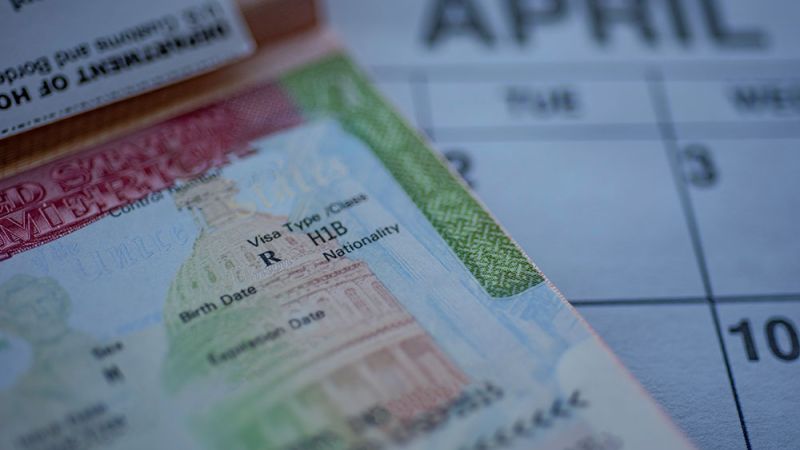 Close-up of an H-1B visa on a passport with a blurred calendar showing the month of April in the background.