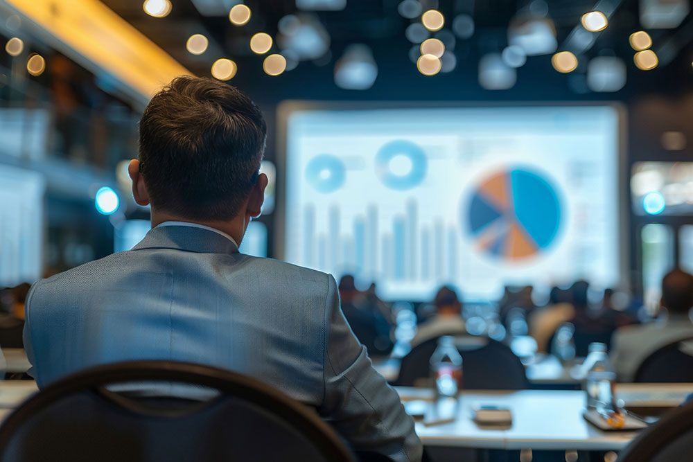 Man in blue suit at a conference, looking at a screen displaying colorful charts and graphs, business presentation setting.