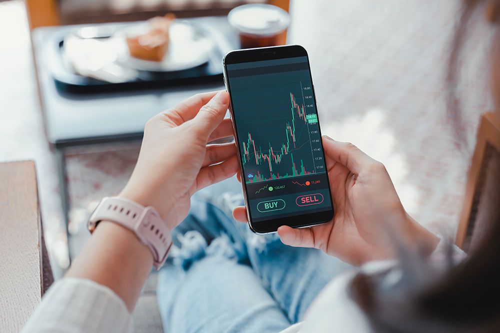 Person analyzing stock market data on a smartphone app, ready to buy or sell stocks.