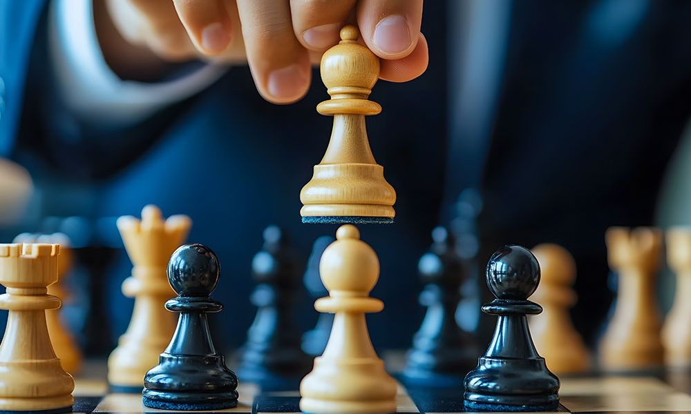 Person moving a white chess piece on a chessboard, symbolizing strategic thinking and decision-making in a game of chess.