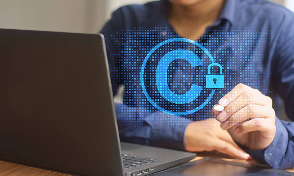Person working on laptop with holographic copyright symbol and padlock, symbolizing digital content protection.