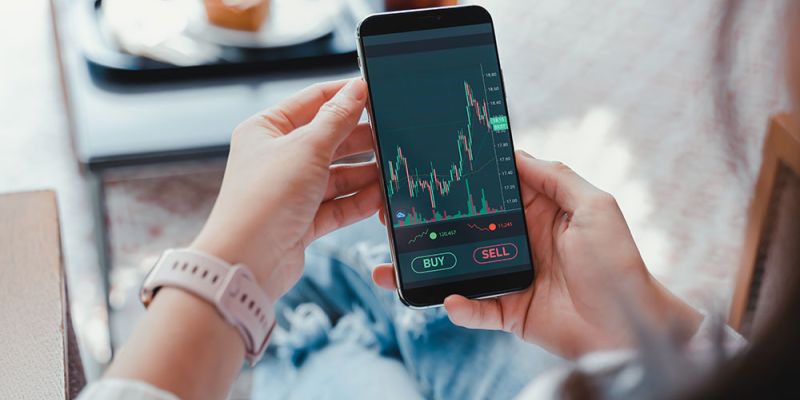 Person analyzing stock market data on a smartphone app, ready to buy or sell stocks.