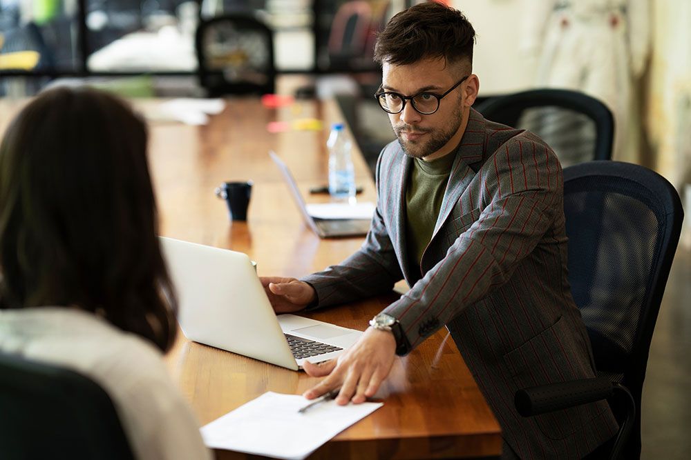 Man in glasses discussing documents with a colleague in a modern office meeting room.