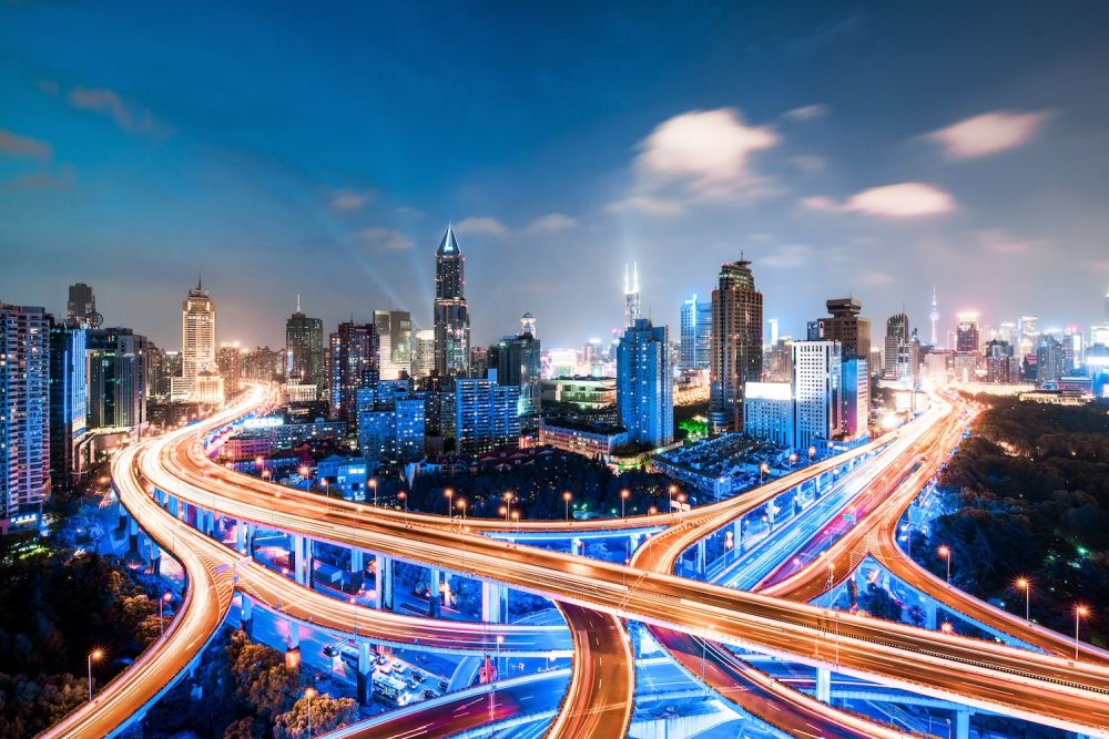 A vibrant cityscape with illuminated highways and tall skyscrapers against a twilight sky.