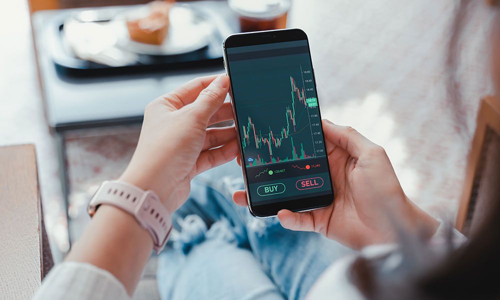 Person analyzing stock market data on a smartphone app, ready to buy or sell stocks.