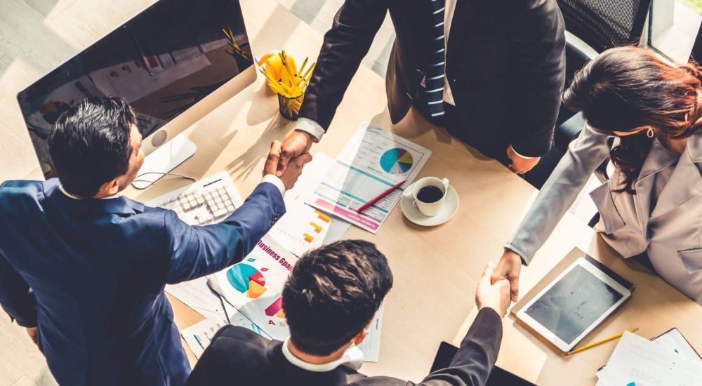 Business meeting with diverse professionals shaking hands over charts, reflecting collaboration and success.